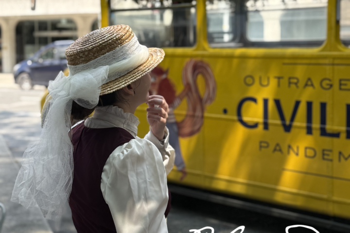Person in vintage attire stands by a yellow bus with 'Bloomsday Festival 11-16 June 2026' text.