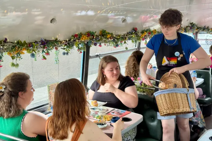 People dining on a decorated double-decker bus, served by a person with a basket.