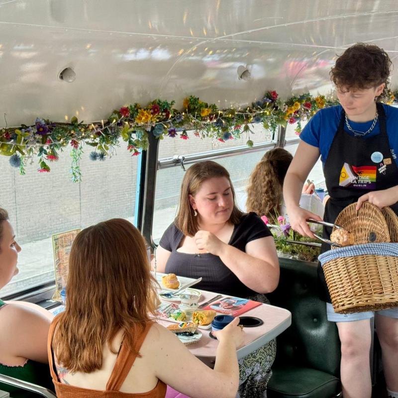 People dining on a decorated double-decker bus, served by a person with a basket.