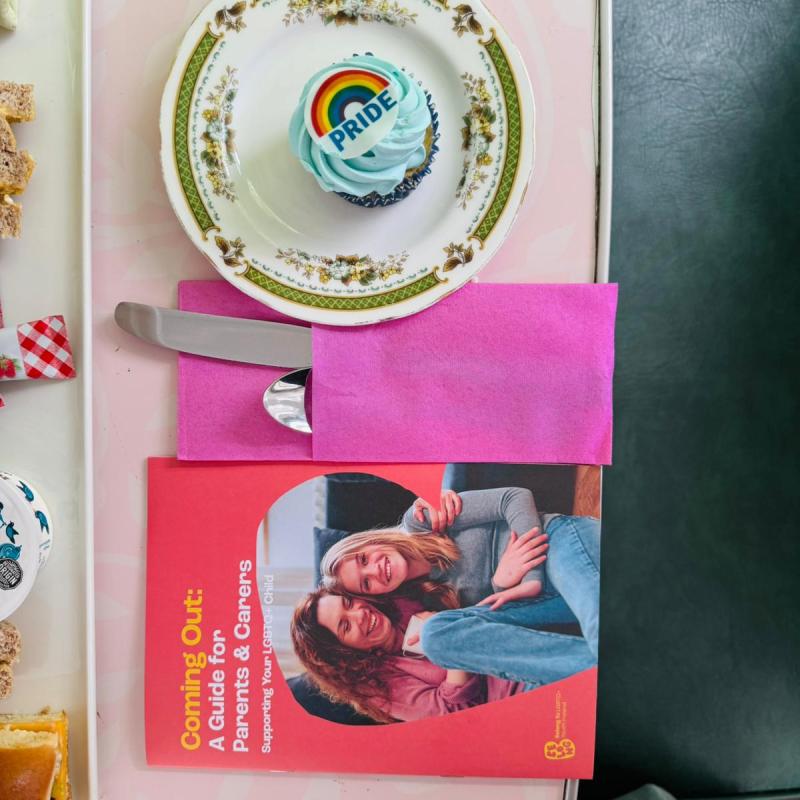 Cupcake with rainbow pride topper on a plate beside a BelongTo booklet.