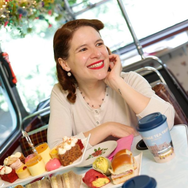 Smiling woman resting arms on bus table with afternoon tea in front of her