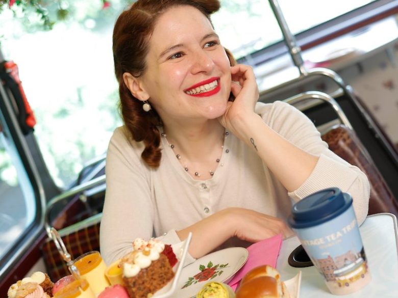 Smiling woman resting arms on bus table with afternoon tea in front of her
