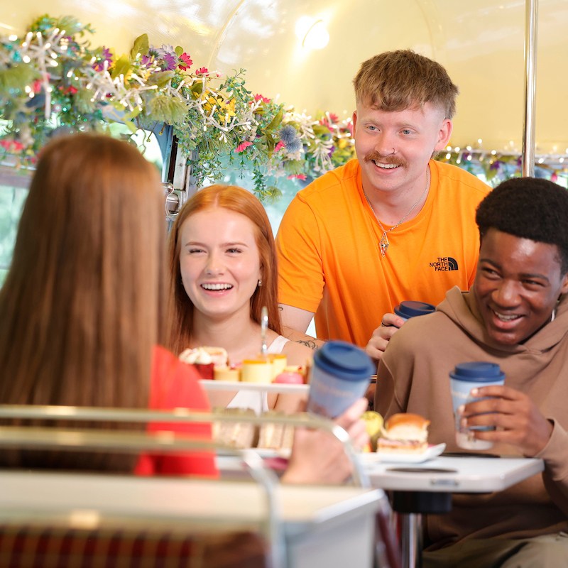 Group of young people on bus laughing and drinking tea together