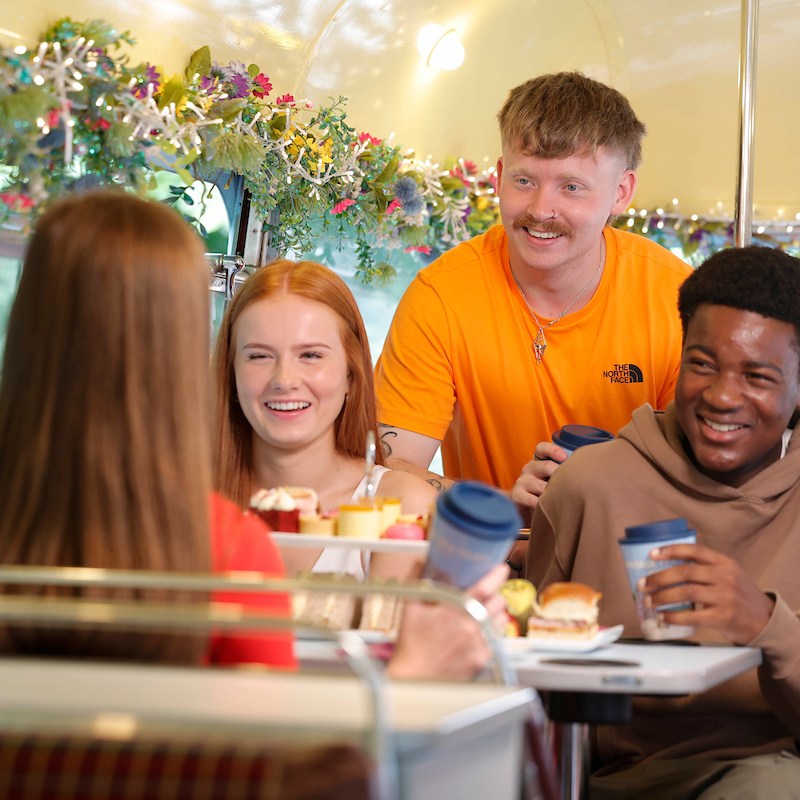 Group of young people laughing together on bus with cups of tea