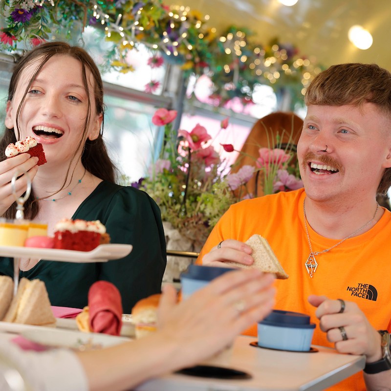 Group of young people seated on bus chatting and eating afternoon tea