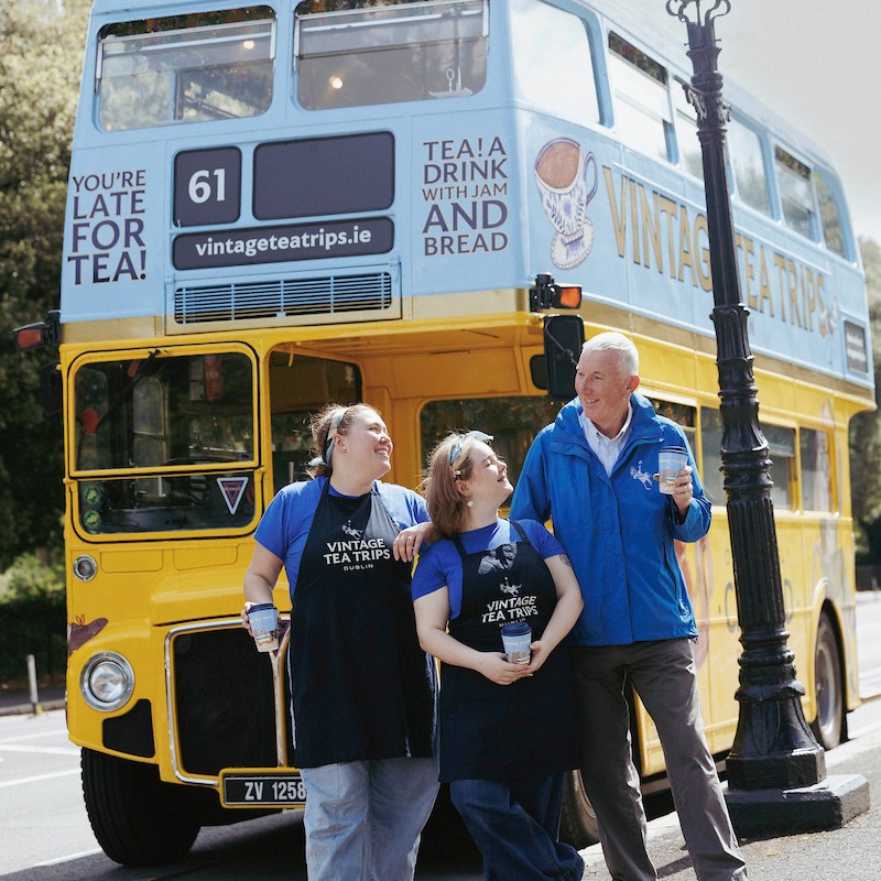 Three Vintage Tea Trips team members holding travel mugs outside the bus