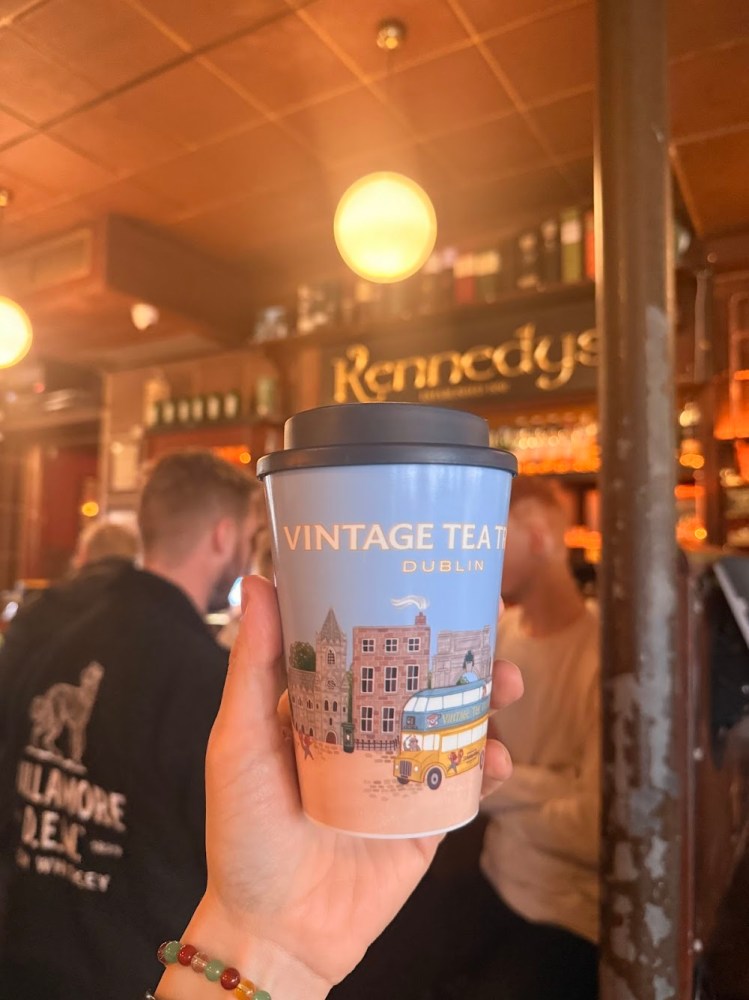 Hand holding a 'Vintage Tea Tours Dublin' cup in a cozy pub setting.