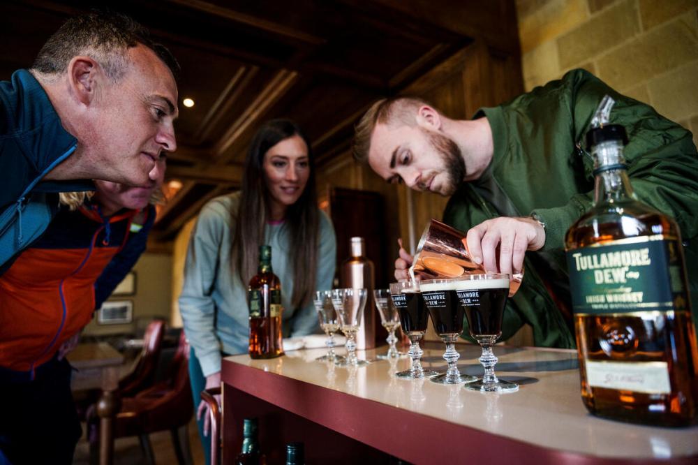 Group watching a man pour drinks into glasses with a Tullamore Dew bottle on the table.