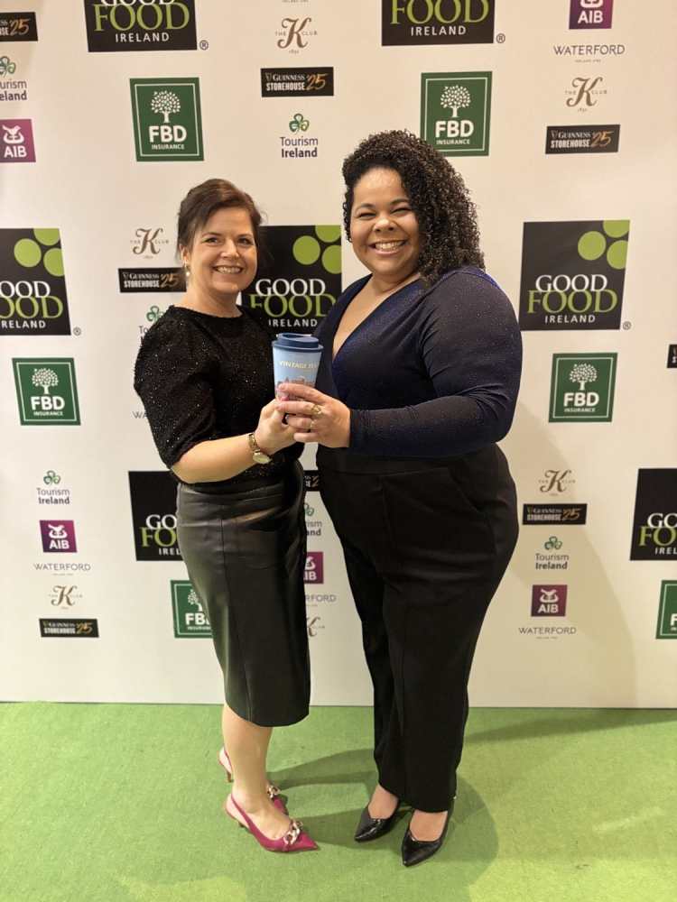 Two women smiling and holding a cup on a Good Food Ireland event backdrop.