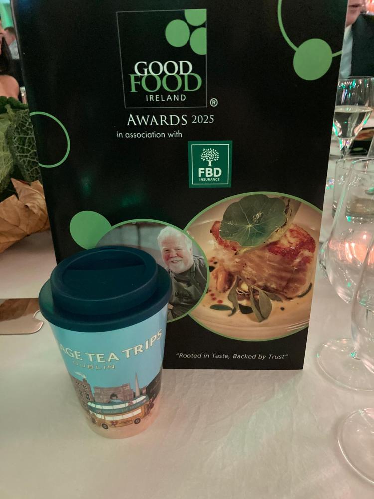 A Good Food Ireland Awards 2025 poster next to a travel-themed cup on a table.