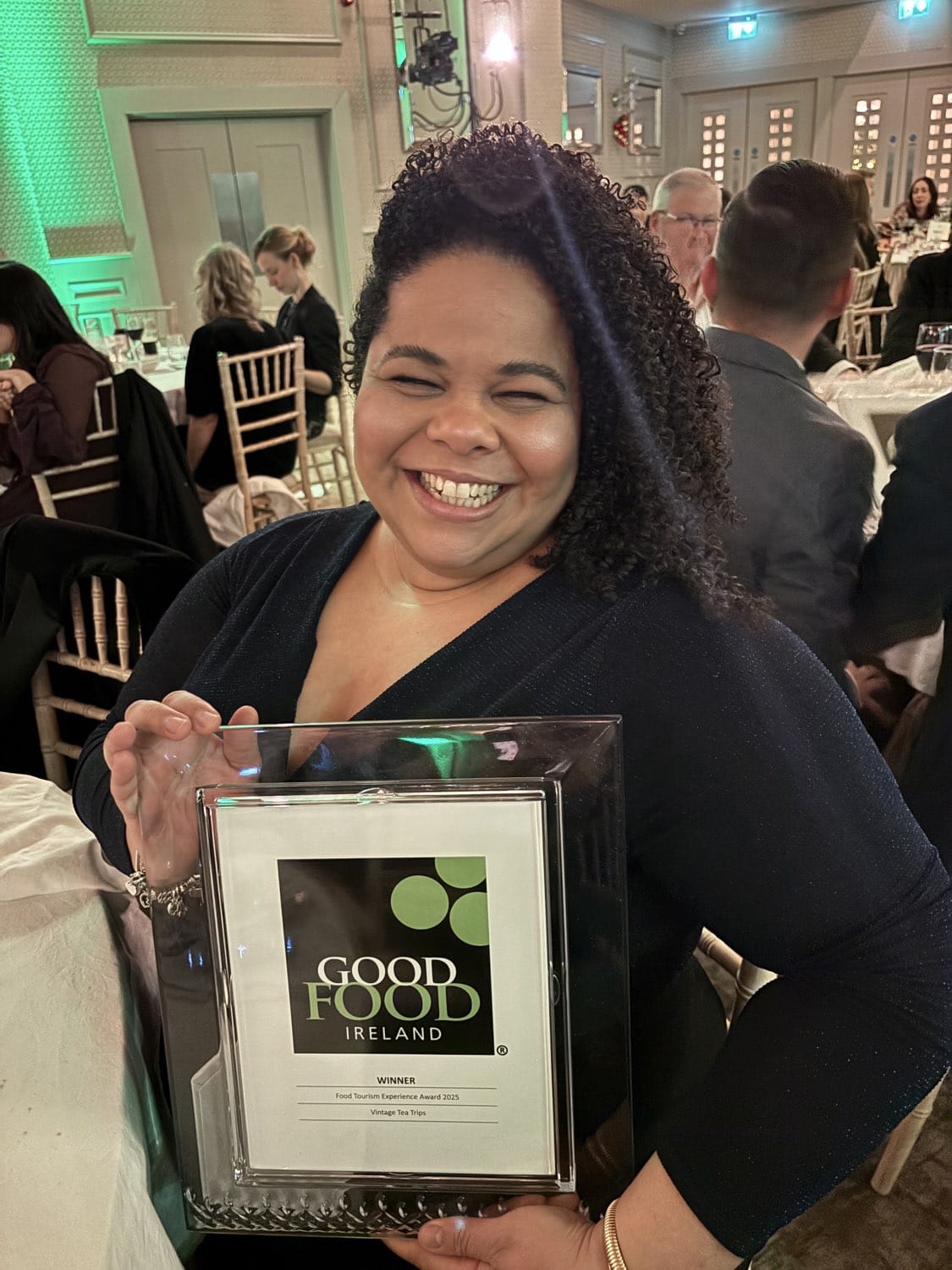 Person smiling and holding a 'Good Food Ireland' award at an indoor event.