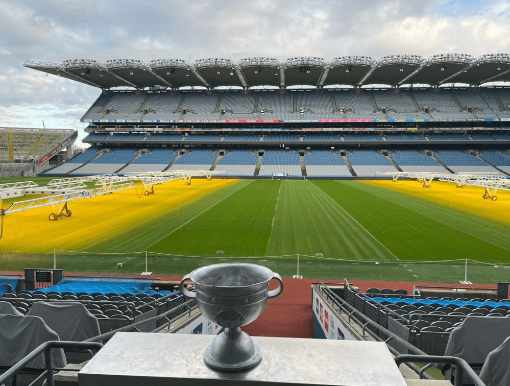 Empty stadium with a trophy in foreground on a table, green field and yellow grow lights.