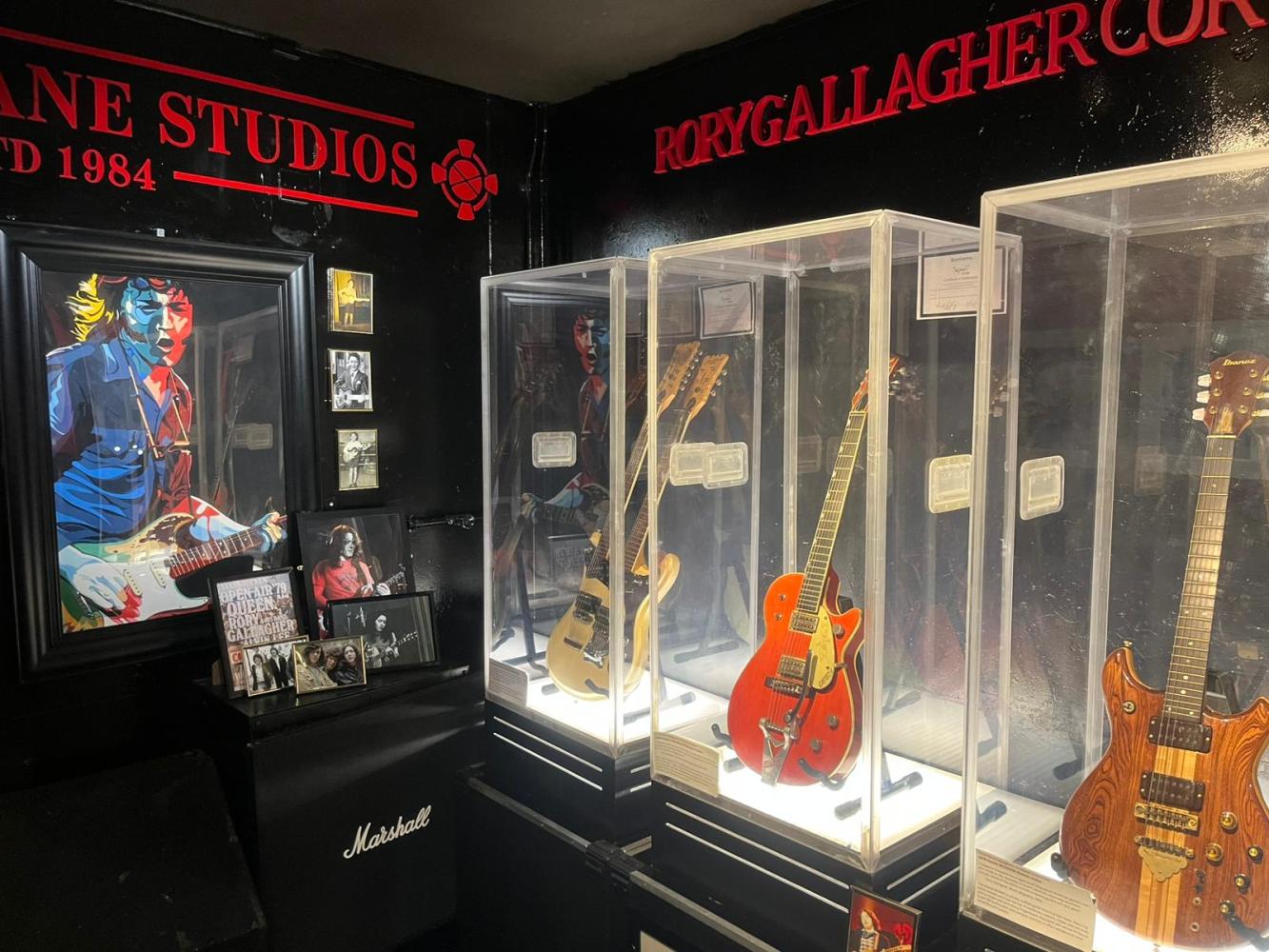 Exhibit featuring guitars in glass cases, wall art, and framed photos in a studio setting.
