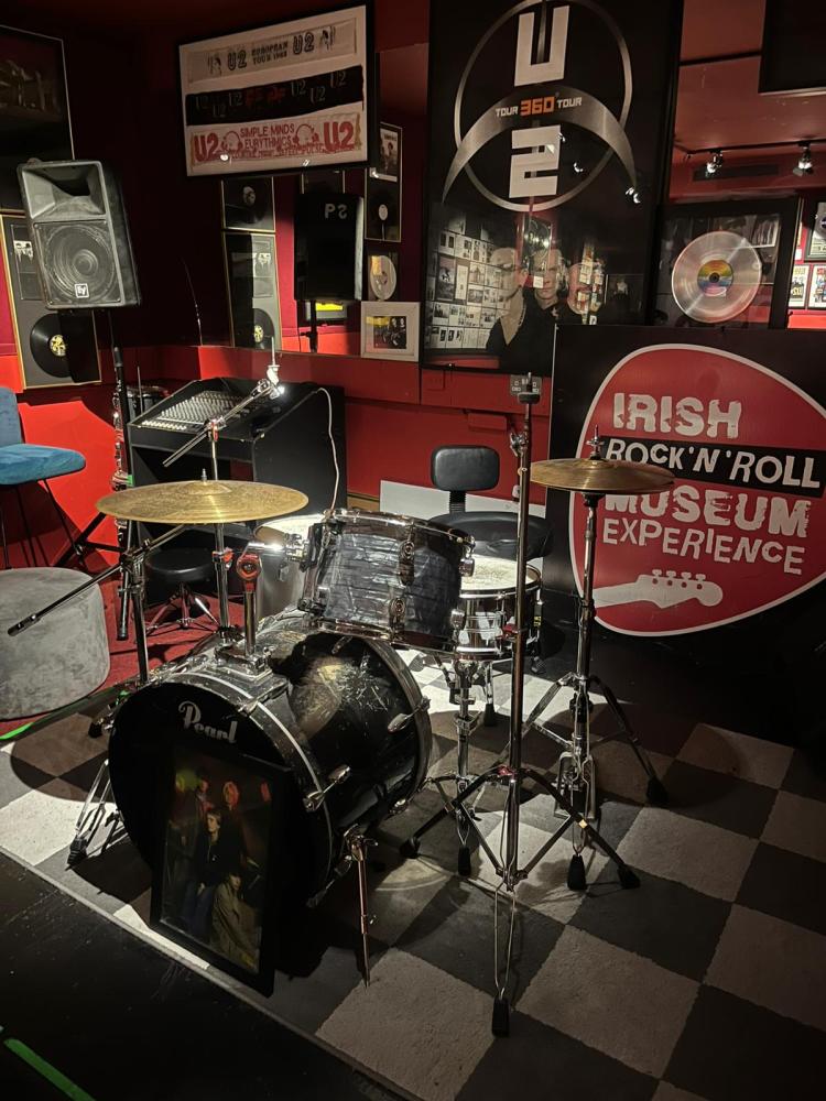 Drum set on checkered floor in music-themed room with posters and memorabilia.