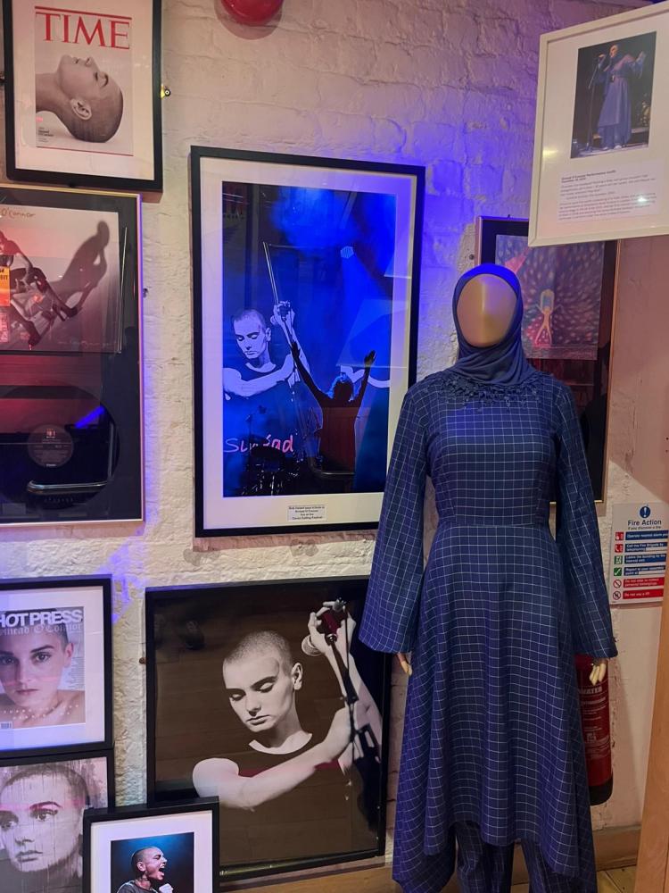Mannequin in blue dress beside framed portraits on wall.