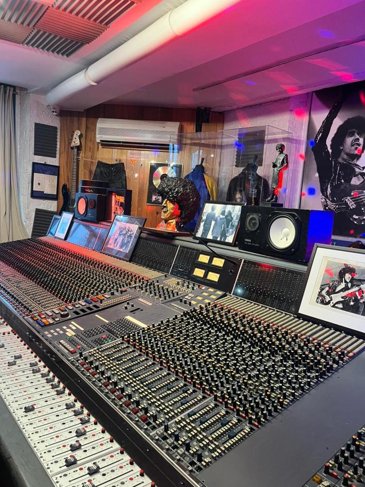 Recording studio with a large mixing console, photos, memorabilia, and colorful lighting.