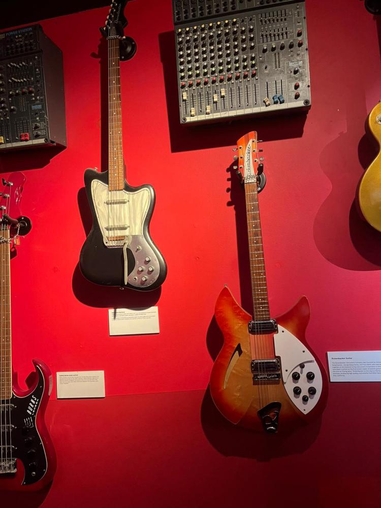 Two electric guitars on a red wall next to a vintage audio mixer.