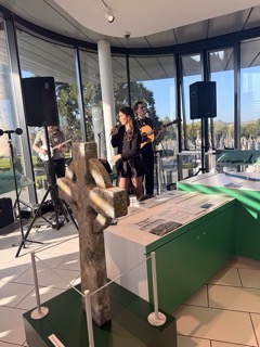 Musicians perform indoors near a stone cross display.