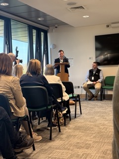 Man speaking at a podium in a conference room with seated audience.