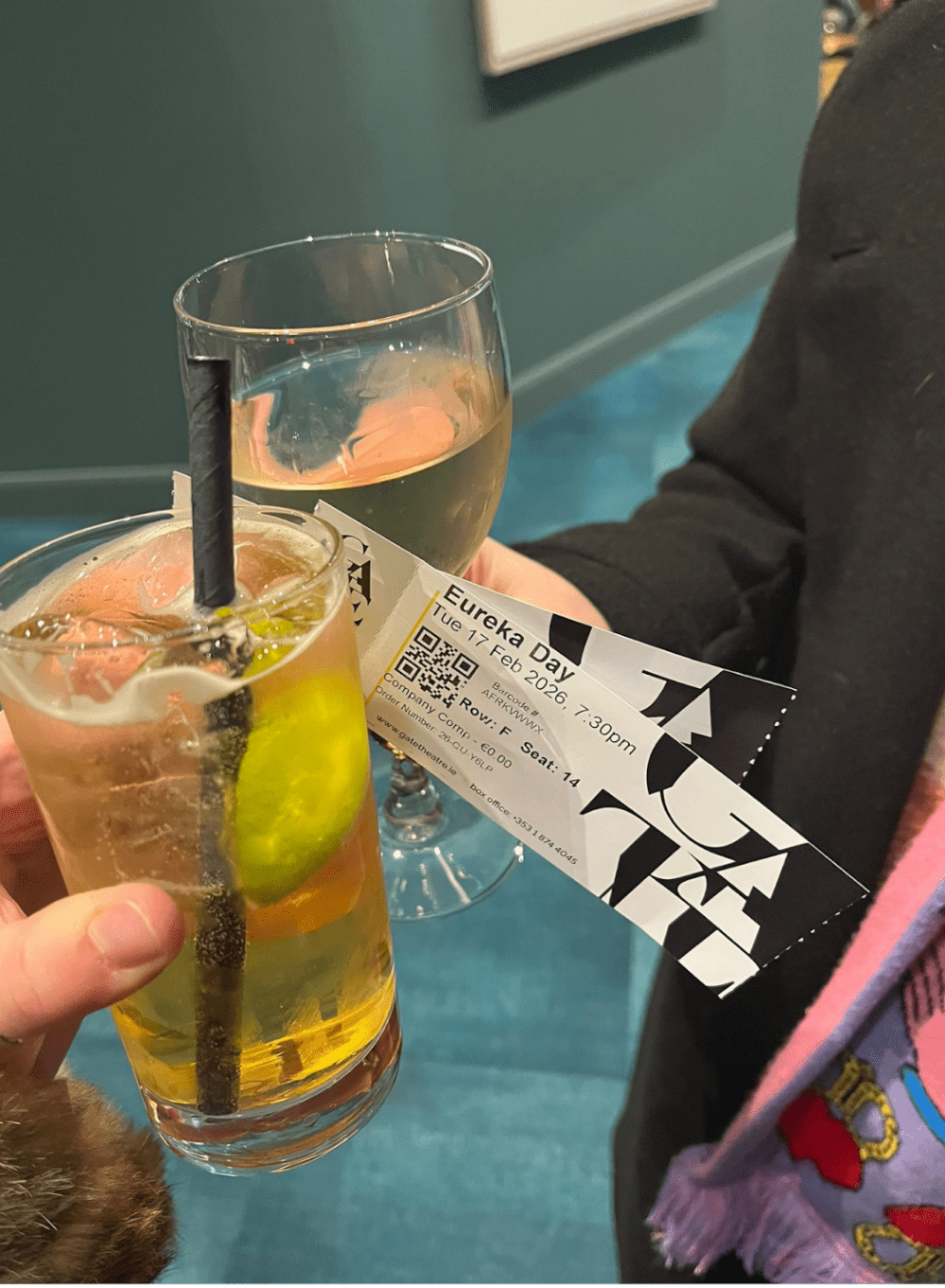 Two people holding drinks and a theater ticket in a blue carpeted room.