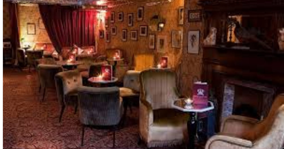 Cozy vintage-style lounge with armchairs, small tables, framed photos, and warm lighting.