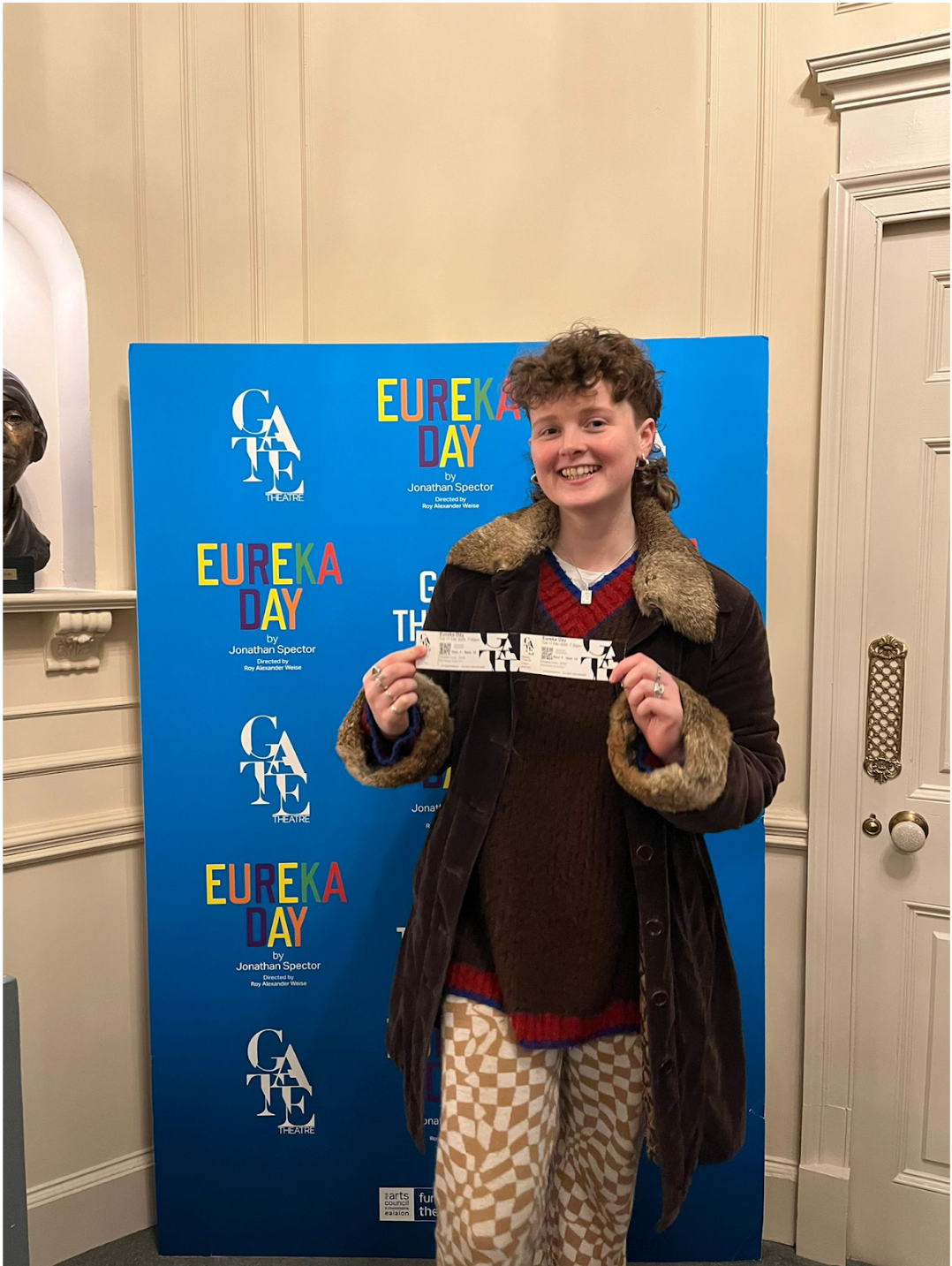 Person holding tickets in front of a blue 'Eureka Day' poster.