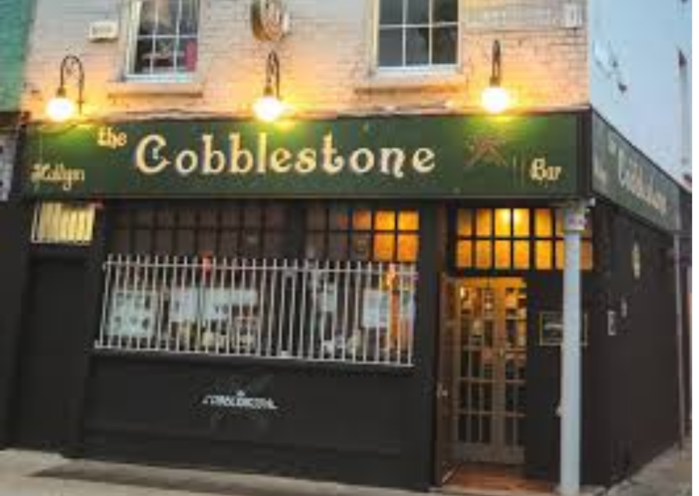 Front view of The Cobblestone bar with lit signage and windows.