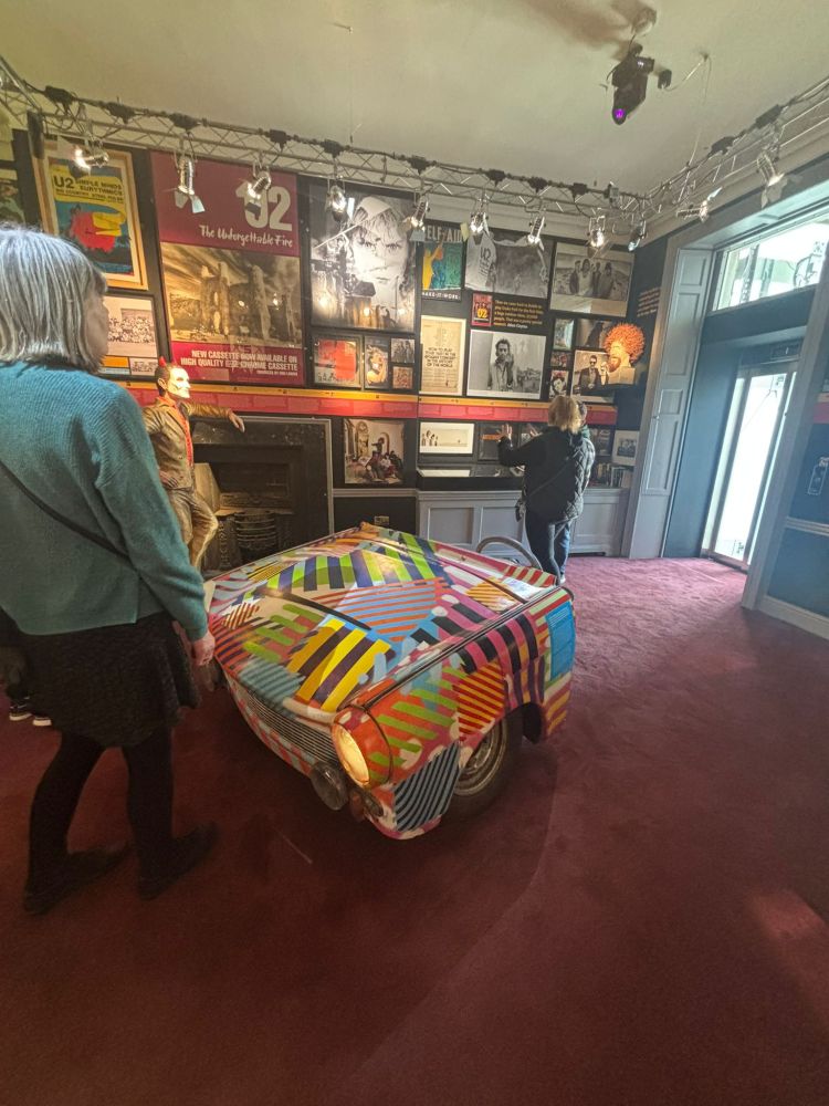 People in a room with colorful car art and music posters on the walls.