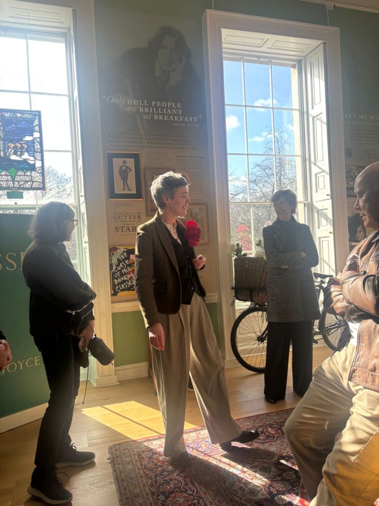 A group of people talking in a sunny room with large windows and wall decorations.
