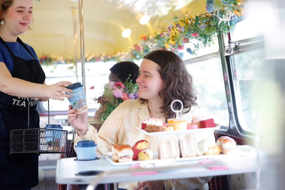 Person seated in a decorated bus receives a drink from a server.