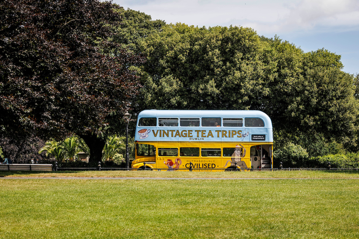Vintage tea bus parked by trees in a park.
