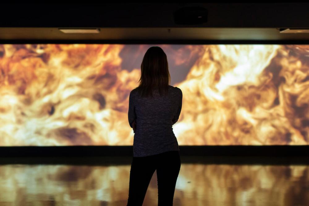 Silhouette of a person facing a large, fiery digital display.