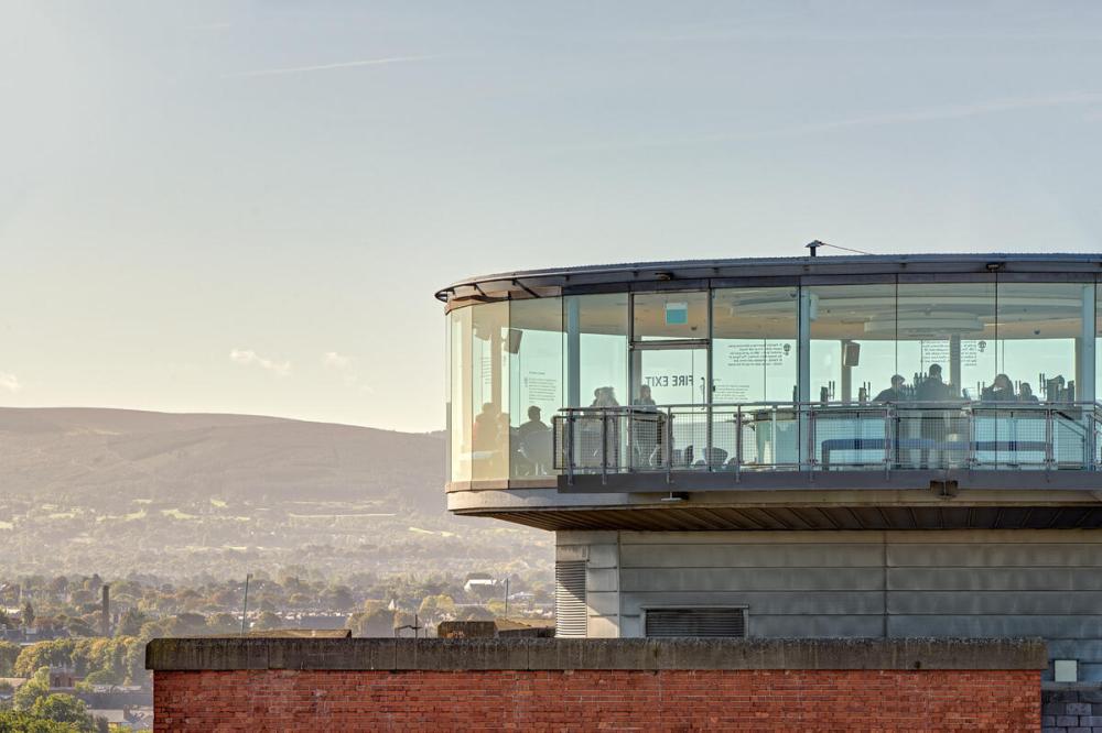 Circular glass observation deck on a building with distant hills in background.
