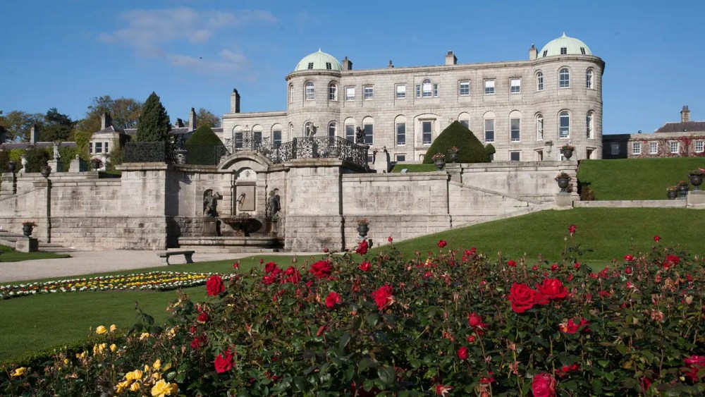 Historic mansion with domes, formal garden, red roses in foreground.