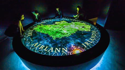 People gathered around an illuminated round map table of Ireland.