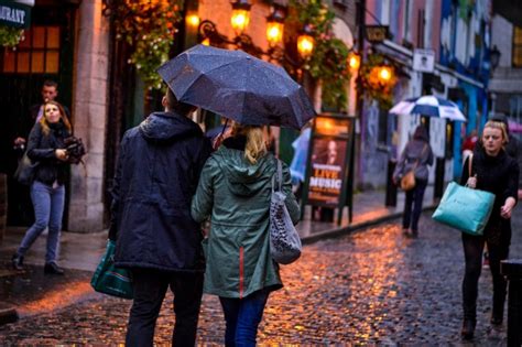 People walking on a rainy cobblestone street with umbrellas and lit storefronts.