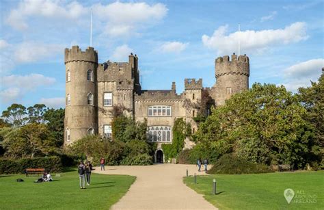 Stone castle with round towers and a tree-lined path in front.