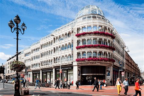 Historic building with glass dome, flowered balconies, street scene with pedestrians.