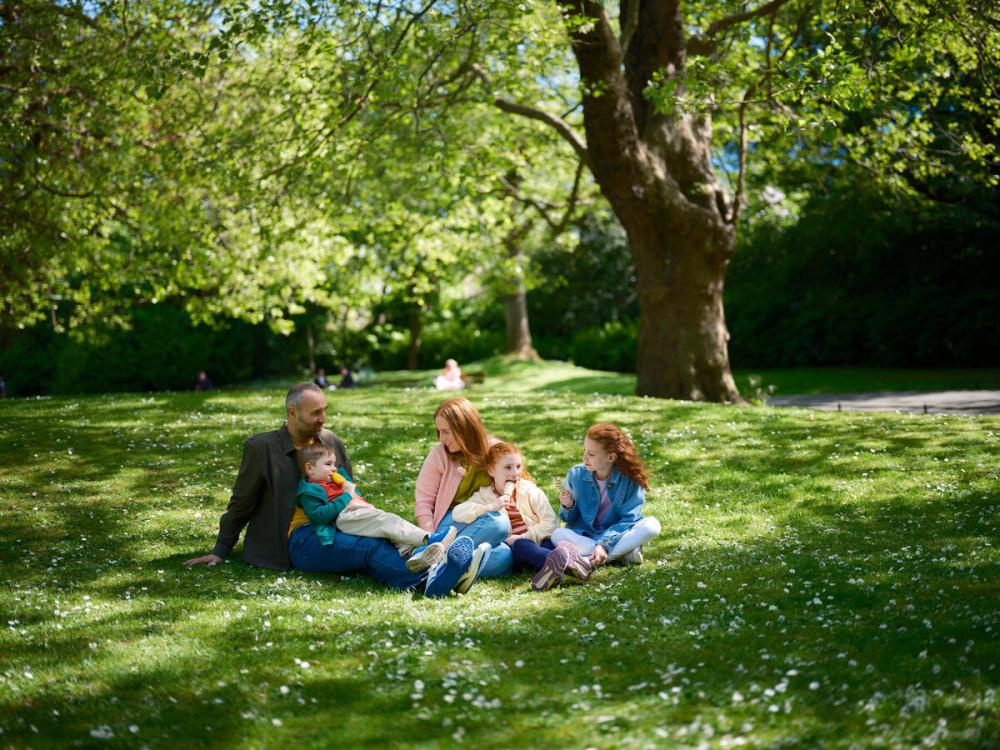 Family sitting on grass in a park under trees on a sunny day.