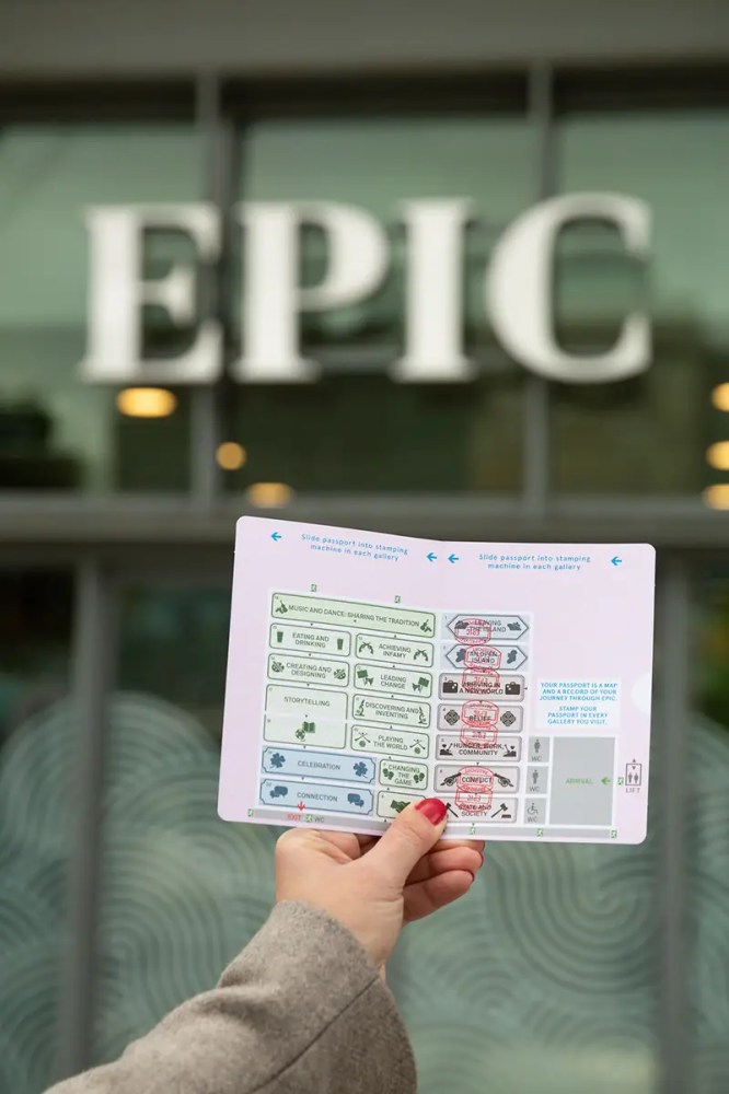 Hand holding a passport page in front of a building with 'EPIC' sign.