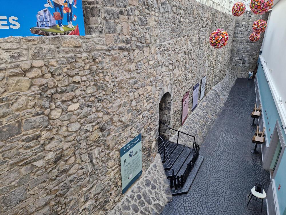 Historic stone wall with posters, decorative spherical ornaments, and cobblestone pathway inside a building.