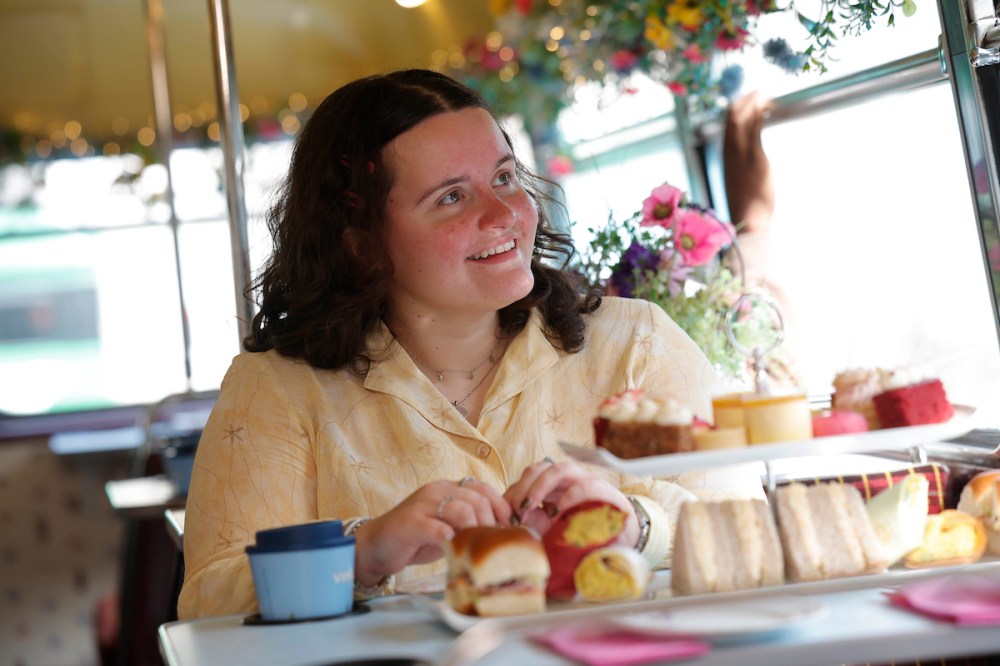 Woman sitting at a table with afternoon tea items and flowers.