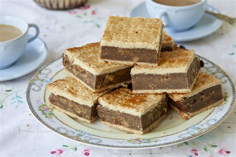 Plate of layered dessert bars with coffee cups on a tablecloth.