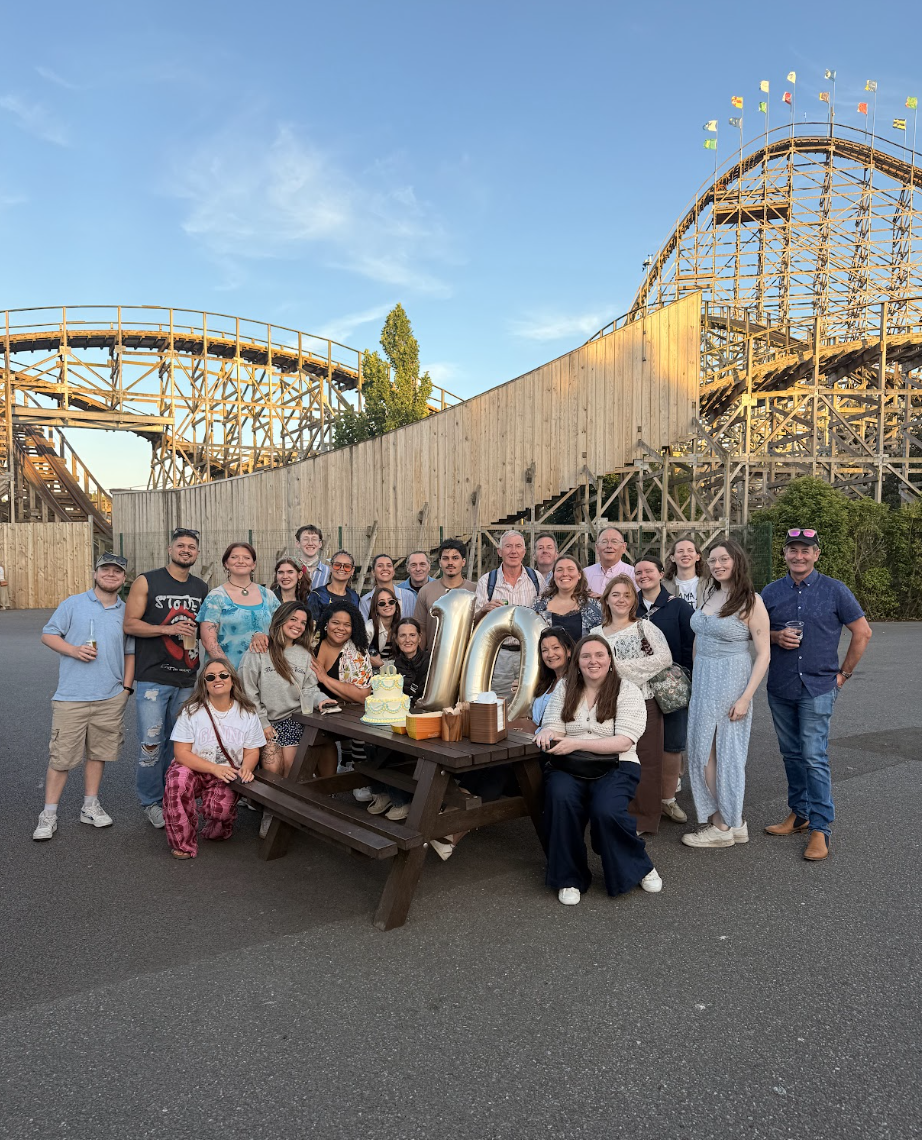 Group of people at picnic table in front of wooden roller coaster.