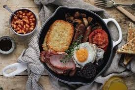 Full English breakfast with eggs, bacon, sausage, beans, and toast on a rustic table.