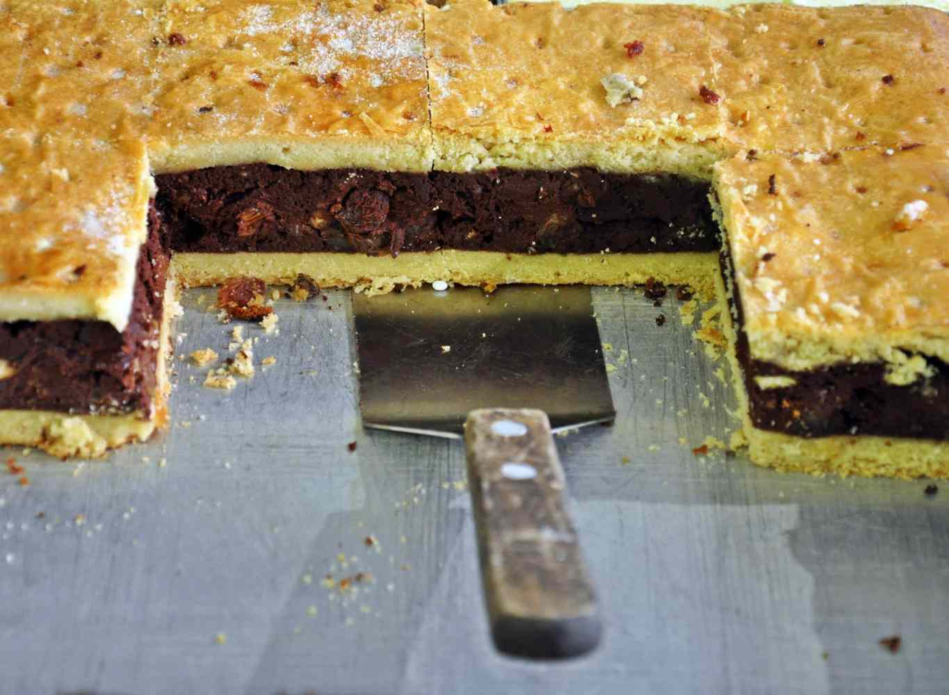 Sliced rectangular pie with chocolate filling on a tray, spatula in front.