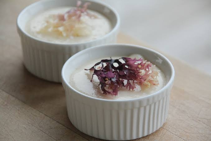 Two small white ramekins with creamy dessert topped with pink and purple edible flowers.