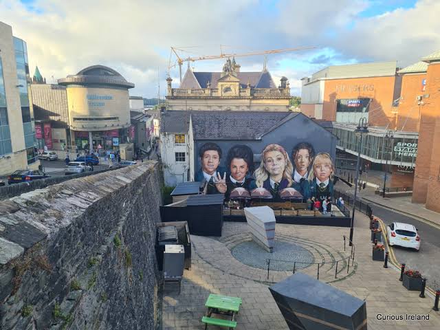 Street view with large mural of six people's faces on building wall in urban area.
