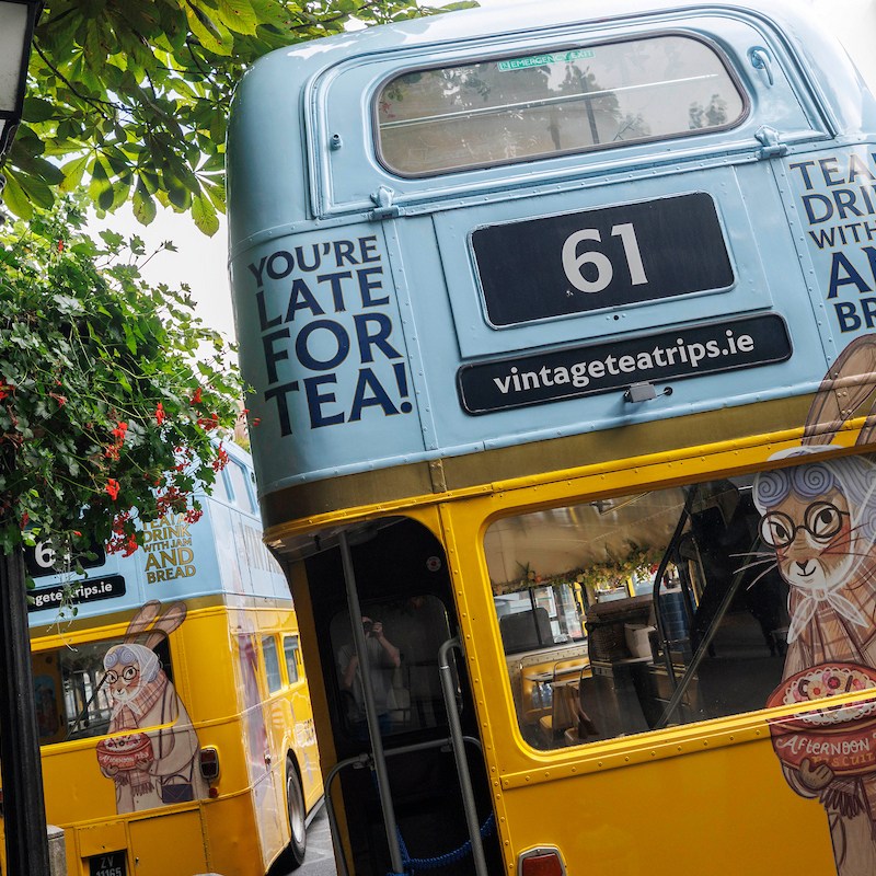 Colorful double-decker buses with tea-themed designs parked under trees.