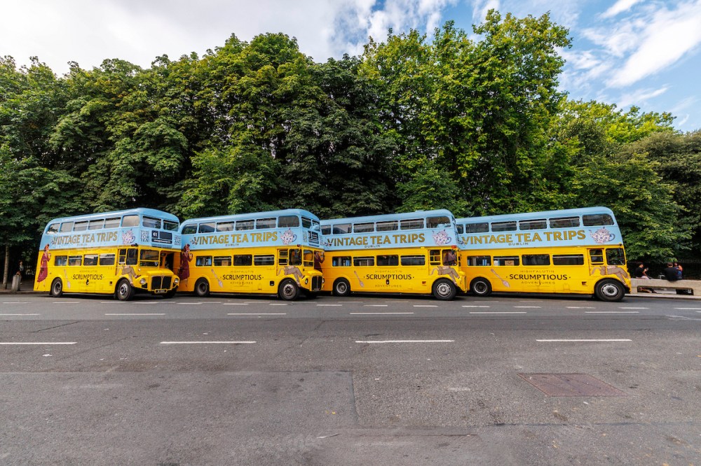 Four vintage double-decker buses parked by trees.